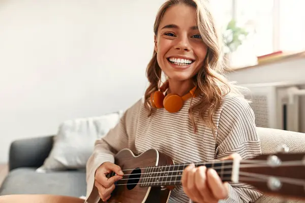 Jovem Feliz Tocando Guitarra Enquanto Senta Sofá Acolhedora Sala Estar — Fotografia de Stock