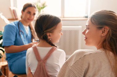 Evde bir aile doktoru, annesi oturma odasındaki kanepede oturan bir çocuğu muayene ediyor. Hasta muayenesi, sağlık ve ilaç.