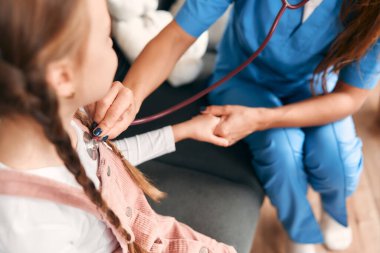 Oturma odasındaki kanepede otururken steteskopla bir çocuğu muayene eden sağlık görevlisi bir kadın çocuk doktoru. Sağlık ve İlaç.