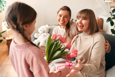 Torunları büyükannelerini tebrik ediyor. Oturma odasındaki kanepede otururken ona çiçek ve hediye veriyorlar. Kadınlar Günü ve Anneler Günü kavramı. Kadın nesli.