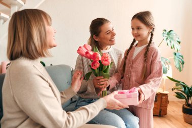 Torunları büyükannelerini tebrik ediyor. Oturma odasındaki kanepede otururken ona çiçek ve hediye veriyorlar. Kadınlar Günü ve Anneler Günü kavramı. Kadın nesli.