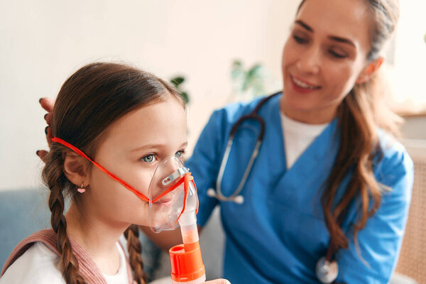 Женщина-педиатр надевает маску для вдыхания на ребенка дома. Обследование пациентов, здравоохранение и медицина.