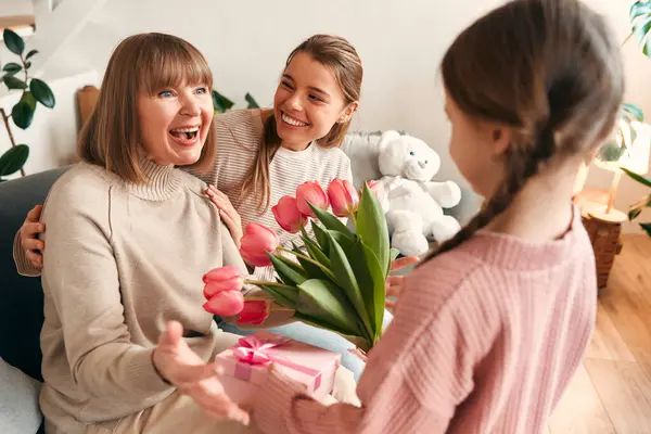 Granddaughter Daughter Congratulating Grandmother Giving Her Flowers Gift While Sitting — Stock Photo, Image