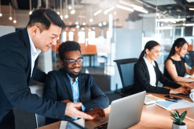 Modern bir ofiste otururken dizüstü bilgisayarlarla çalışan takım elbiseli genç iş adamları. Çalışanlar bir dizüstü bilgisayarda çalışma planı ya da projeyi tartışıyor.