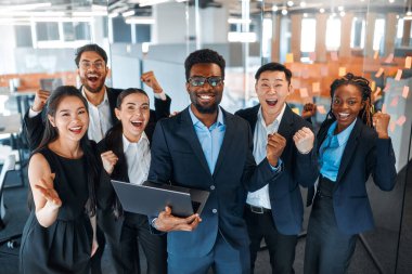 Farklı uluslardan başarılı iş adamlarından oluşan bir ekip zaferi, başarıyı modern bir ofiste dururken kutluyor..