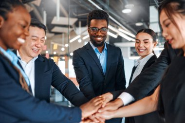 Farklı uluslardan başarılı iş adamlarından oluşan bir ekip zaferi kutluyor. Elleri birbirine kenetlenmiş modern bir ofiste dururken başarı kazanıyorlar..