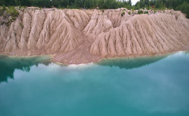 Dağların ve ağaçların arasına yerleşmiş bir göl manzarası. Uçsuz bucaksız gökyüzünün altında yemyeşil bir lacustrine ovasından akan bir su yolu.
