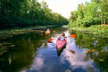 Ukrayna 'nın Kiev kentindeki Dinyeper Nehri' nde ormanın yakınlarındaki nilüferlerin arasında kayak yapan iki genç kız. Turizm ve dinlenme.