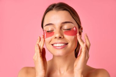 Gözlerinin altında nemlendirici bantları olan güzel bir kadın pembe arka planda izole edilmiş. Yüz bakımı, kozmetoloji, güzellik konsepti..