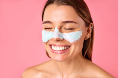 Güzel, mutlu bir kadın siyah noktalar ve pembe arka planda izole edilmiş büyümüş gözenekler için yüz maskesi kullanıyor. Cilt bakımı, kozmetoloji, güzellik konsepti.