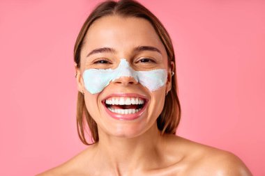 Güzel, mutlu bir kadın siyah noktalar ve pembe arka planda izole edilmiş büyümüş gözenekler için yüz maskesi kullanıyor. Cilt bakımı, kozmetoloji, güzellik konsepti.