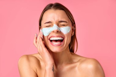 Güzel, mutlu bir kadın siyah noktalar ve pembe arka planda izole edilmiş büyümüş gözenekler için yüz maskesi kullanıyor. Cilt bakımı, kozmetoloji, güzellik konsepti.