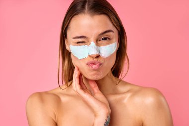 Güzel, mutlu bir kadın siyah noktalar ve pembe arka planda izole edilmiş büyümüş gözenekler için yüz maskesi kullanıyor. Cilt bakımı, kozmetoloji, güzellik konsepti.