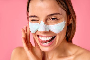 Güzel, mutlu bir kadın siyah noktalar ve pembe arka planda izole edilmiş büyümüş gözenekler için yüz maskesi kullanıyor. Cilt bakımı, kozmetoloji, güzellik konsepti.