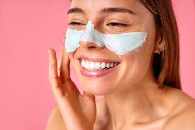 Güzel, mutlu bir kadın siyah noktalar ve pembe arka planda izole edilmiş büyümüş gözenekler için yüz maskesi kullanıyor. Cilt bakımı, kozmetoloji, güzellik konsepti.