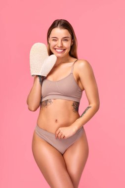 İç çamaşırlı zayıf bir kadın pembe arka planda izole edilmiş anti-selülit eldiven kullanarak vücudun sorunlu bölgelerine masaj yapıyor. Vücut bakımı. Spa tedavileri ve kozmetoloji.