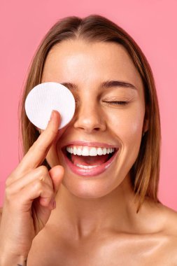 Beyaz tenli beyaz bir kadın pamuk pedlerle yüzünü tonerle siliyor ya da pembe arka planda izole edilmiş makyajı kaldırıyor. Yüz bakımı. Spa tedavileri ve kozmetoloji.