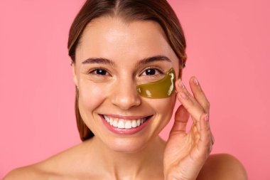 Gözlerinin altında nemlendirici bantları olan güzel bir kadın pembe arka planda izole edilmiş. Yüz bakımı, kozmetoloji, güzellik konsepti..