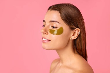 Gözlerinin altında nemlendirici bantları olan güzel bir kadın pembe arka planda izole edilmiş. Yüz bakımı, kozmetoloji, güzellik konsepti..