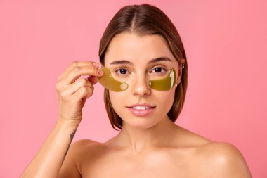 Gözlerinin altında nemlendirici bantları olan güzel bir kadın pembe arka planda izole edilmiş. Yüz bakımı, kozmetoloji, güzellik konsepti..