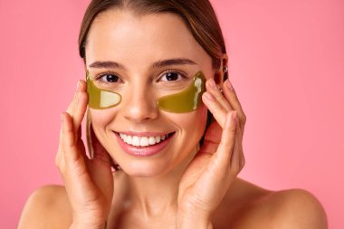 Gözlerinin altında nemlendirici bantları olan güzel bir kadın pembe arka planda izole edilmiş. Yüz bakımı, kozmetoloji, güzellik konsepti..