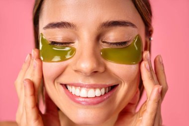 Gözlerinin altında nemlendirici bantları olan güzel bir kadın pembe arka planda izole edilmiş. Yüz bakımı, kozmetoloji, güzellik konsepti..