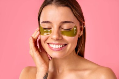 Gözlerinin altında nemlendirici bantları olan güzel bir kadın pembe arka planda izole edilmiş. Yüz bakımı, kozmetoloji, güzellik konsepti..