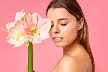 Güzel bakımlı, pırıl pırıl sağlıklı bir kadın pembe arka planda izole edilmiş bir çiçek tutuyor. Yüz bakımı, kozmetoloji, güzellik konsepti..