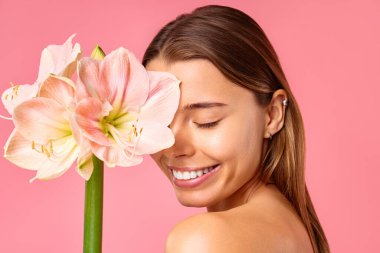 Güzel bakımlı, pırıl pırıl sağlıklı bir kadın pembe arka planda izole edilmiş bir çiçek tutuyor. Yüz bakımı, kozmetoloji, güzellik konsepti..