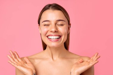 Neşeli genç bir kadın pembe bir arka planda parlak bir gülümseme sergiliyor, parlak cildini ve doğal güzelliğini sergiliyor. Sağlık, cilt bakımı ve pozitiflik için mükemmel..