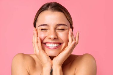 Neşeli genç bir kadın pembe bir arka planda parlak bir gülümseme sergiliyor, parlak cildini ve doğal güzelliğini sergiliyor. Sağlık, cilt bakımı ve pozitiflik için mükemmel..
