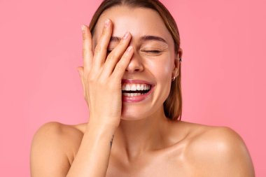 Neşeli genç bir kadın pembe bir arka planda parlak bir gülümseme sergiliyor, parlak cildini ve doğal güzelliğini sergiliyor. Sağlık, cilt bakımı ve pozitiflik için mükemmel..