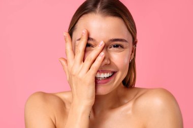Neşeli genç bir kadın pembe bir arka planda parlak bir gülümseme sergiliyor, parlak cildini ve doğal güzelliğini sergiliyor. Sağlık, cilt bakımı ve pozitiflik için mükemmel..