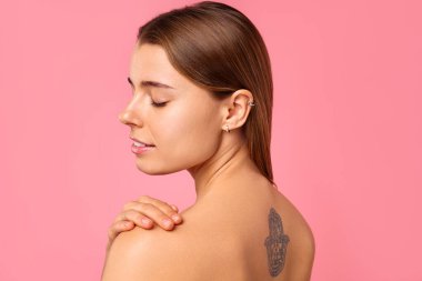 Genç bir kadın, sırtında pembe bir dövme sergiliyor. Bu sanatsal vücut sanatında memnuniyet ve rahatlama yayıyor.