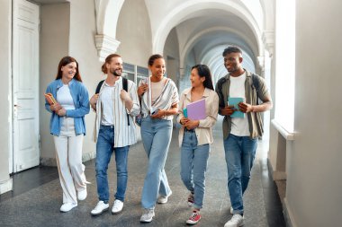 Çeşitli beş öğrenciden oluşan bir grup, bir üniversite koridorunda arkadaşlıklarını ve takım çalışmalarını sergileyerek, bir üniversite ortamında akademik işbirliği ruhunu somutlaştırarak mutlu bir şekilde yürüyorlar.