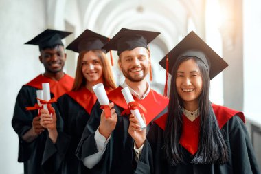 Bir grup farklı, neşe dolu mezunlar akademik başarılarını bir mezuniyet töreninde kutluyor, mutluluk ve memnuniyet saçan diplomalarını gururla gösteriyorlar.