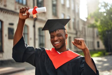 Şapkalı ve cüppeli genç bir adam akademik başarısını dışarıda kutluyor. Diplomasını güneş ışığında gururla tutuyor. Başarısı için gururunu ve mutluluğunu neşeyle ifade ediyor.