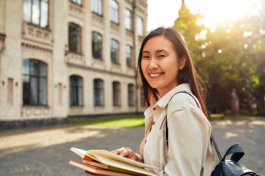 Gün batımında, bir üniversite öğrencisi üniversite binasının yakınındaki açık havada kitap okumaktan zevk alıyor. Omuzlarında bir sırt çantasıyla kampüsün sakin atmosferine karışıyor.