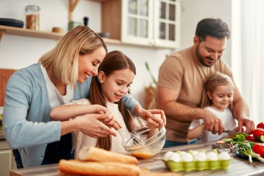 Neşeli bir aile, güzel bir mutfakta taze sebzelerle yemek pişirmek, kaynaşmak ve eğlenmek için bir araya gelir.