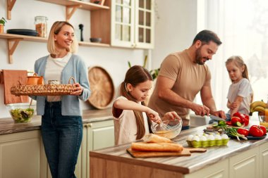 Mutlu bir aile, parlak bir mutfakta birlikte yemek pişiriyor, neşe, takım çalışması ve ev yemeği sevgisini gösteriyor, evde sıcak ve sevgi dolu bir atmosfer yaratıyor.