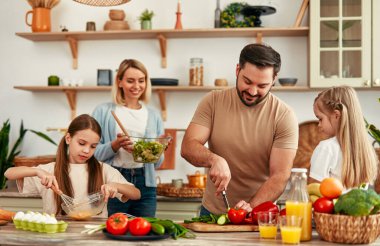 Mutlu bir aile, parlak bir mutfakta birlikte yemek pişiriyor, neşe, takım çalışması ve ev yemeği sevgisini gösteriyor, evde sıcak ve sevgi dolu bir atmosfer yaratıyor.