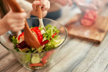 Sıcak bir mutfakta, ebeveynler ve çocuklar taze bir sebze salatası hazırlarken, aile zamanlarını el üstünde tutarken ve sıcak bir atmosferde birlikte yemek pişirirken birbirlerine bağlanırlar.