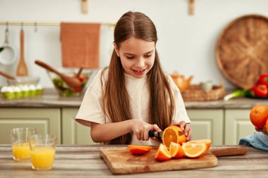 İki çocuk parlak mutfakta meyve suyu yapmak için portakal kesiyor, ev yapımı iyilik etrafında mutlu ve sağlıklı bir aile yaşam tarzını sembolize ediyorlar.