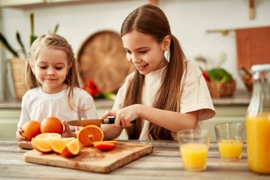 İki çocuk parlak mutfakta meyve suyu yapmak için portakal kesiyor, ev yapımı iyilik etrafında mutlu ve sağlıklı bir aile yaşam tarzını sembolize ediyorlar.