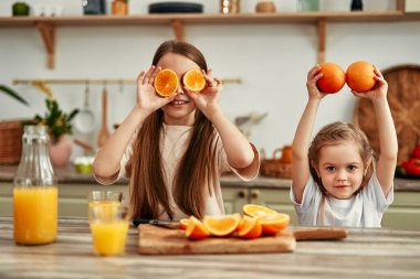 İki çocuk parlak mutfakta meyve suyu yapmak için portakal kesiyor, ev yapımı iyilik etrafında mutlu ve sağlıklı bir aile yaşam tarzını sembolize ediyorlar.
