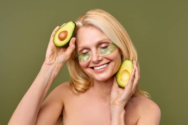 Avokadosu olan sakin bir kadın yeşil göz bandı takar. Güzellik rutininde bir anlık rahatlama ve kendine özen göstererek cilt sağlığını iyileştirmeye çalışır.