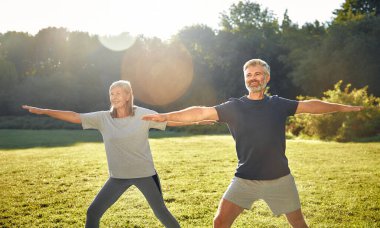 Güneşli güzel bir parkta, olgun bir çift çeşitli yoga pozları vererek, doğa ve arkadaşlığın tadını çıkarırken, dışarıda huzurlu bir ortamda sağlık, sağlık ve farkındalığı teşvik ederler.