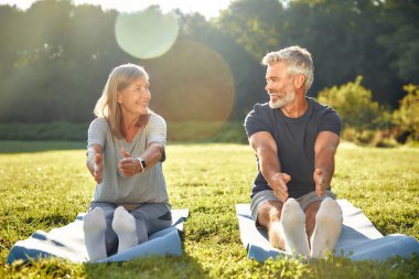 Güneşli güzel bir parkta, olgun bir çift çeşitli yoga pozları vererek, doğa ve arkadaşlığın tadını çıkarırken, dışarıda huzurlu bir ortamda sağlık, sağlık ve farkındalığı teşvik ederler.