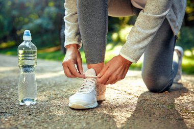 Bir insan doğanın dışında diz çöküp, koşan ayakkabısını özenle bağlıyor, yakınına yerleştirilmiş bir su şişesi ile, günlük olarak kucakladıkları sağlıklı ve aktif yaşam tarzını mükemmel bir şekilde gösteriyor.