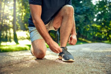 Kendini adamış bir koşucu, ayakkabı bağcıklarını güneşli bir yolda dikkatlice bağlamak için diz çöker ve yakınına bir su şişesi yerleştirir. Bu da onu çeşitli spor ve fitness temaları için ideal bir sahne haline getirir.